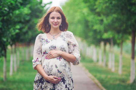 Cute pregnant woman in lace tunic walks outdoors in summer gardenの写真素材
