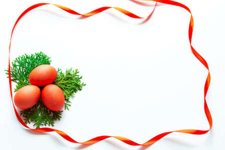 Postcard with three red Easter eggs that lie on green thuja sprigs and around colored satin ribbons on a white backgroundの写真素材