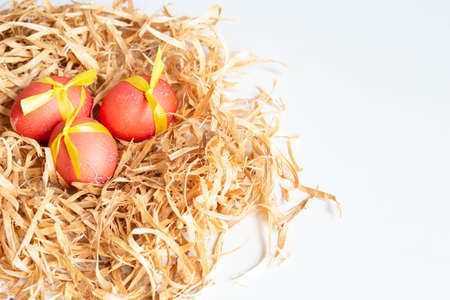 Decorated red Easter eggs lie in a nest made of wood shavings on a white background close-up....