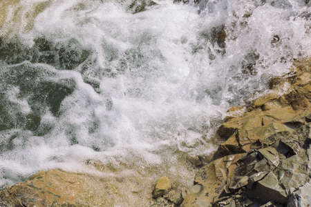 mountain blue water flows down from gray stones waterfall in summer close-up