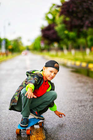 teenager in cap and green jacket rides blue skateboard on the roadの写真素材