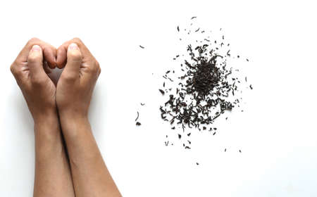 a handful of dry black tea and female hands making a heart shaped gesture on a white backgroundの写真素材