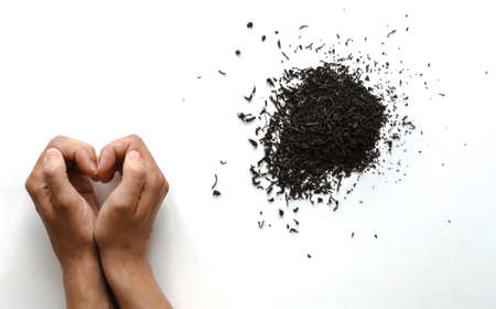 a handful of dry black tea and female hands making a heart shaped gesture on a white backgroundの写真素材