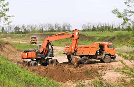 excavator at a construction site against the backdrop of a sunset sky and green trees and grass
