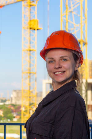 Beautiful girl in a red protective helmet with a smile on her face. Happy BUILDER. Construction site...