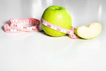 solated green apple with dew drop and apple slice and on white table. Measuring tape on the appleの写真素材
