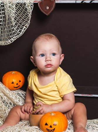 A small baby is sitting next to a pumpkin in a brown chest.の写真素材