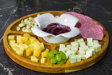 Cheese platter with fresh grapes and nuts on a brown table. View from above.