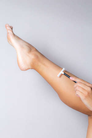 female hand shaves leg with disposable razor on white background