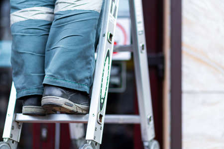 A worker in boots and a hazmat suit climbs an aluminum ladderの写真素材