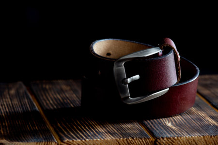 Close-up of a leather belt on a wooden surface on a blurred black background