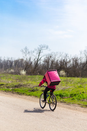 A courier in a thermal backpack rides a bicycle off-road to deliver orders to customers and customersの写真素材