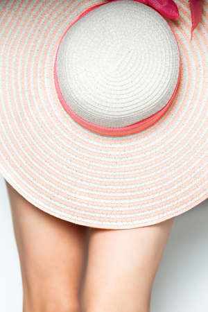 Bare female legs covered with a straw beach hat with a brim on a white background