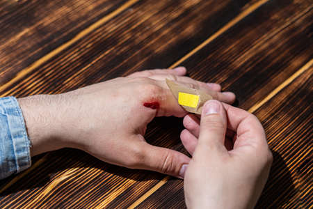 Close-up of a male hand with a bloody wound and a plaster-aid on a wooden backgroundの写真素材