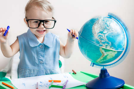 A little girl in glasses smiles against the background of a globe and album sheets with markersの写真素材