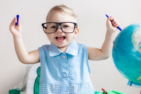 Blurred little girl in glasses smiles against the background of a blurred globe and album sheets with markers.の写真素材
