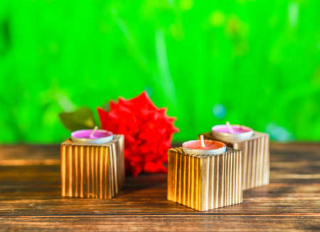 Close-up of wooden candle holders with tea light on red rose petals and blurred green background.の写真素材