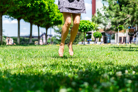 blurred naked female legs on tiptoe jumping barefoot against the background of greenery in the parkの写真素材