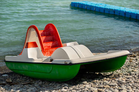Green catamaran on a pebble beach against the background of the sea.