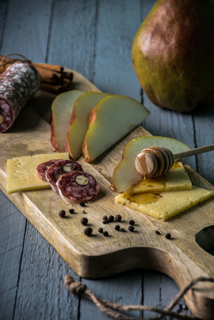 cheese with slices of pear, salami and honey on wooden cutting boardの写真素材