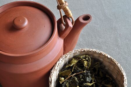 A clay teapot with a small basket of dried tea leaves by its side.の写真素材