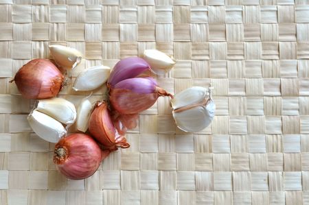 Several onions and garlics rest on a grass mat.の写真素材