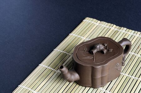 A small clay teapot rests on a bamboo mat.の写真素材