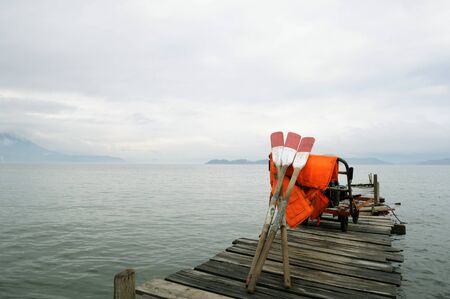 A cart carrying several oars and life jackets rests on a wooden jetty.の写真素材