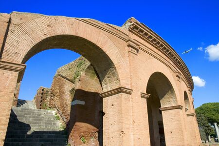 a plane landing in the blue sky above the ancient Ostia Antica Theaterの写真素材