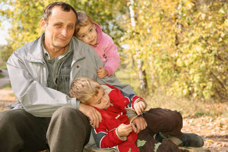 grandfather with the grandson and the granddaughter in the park in autumnの写真素材