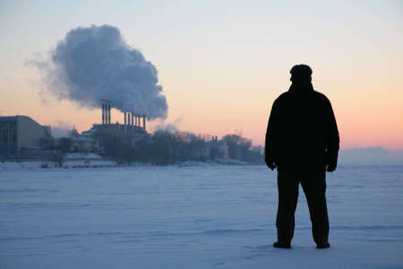man stand on the frozen river near smoking pipesの写真素材