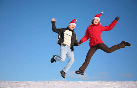 couple jump on snow in santa claus hatsの写真素材