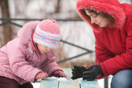 mother with child play with snow on benchの写真素材