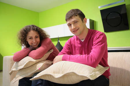 couple sit on sofa with pillows in green roomの写真素材