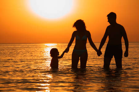 Parents with child in sea on sunsetの写真素材