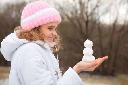 young beauty girl outdoor in winter holds small snowman in handsの写真素材
