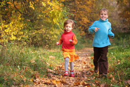 Two children run on wood autumn footpathの写真素材