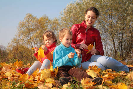 Mother with children sit on fallen maple leavesの写真素材