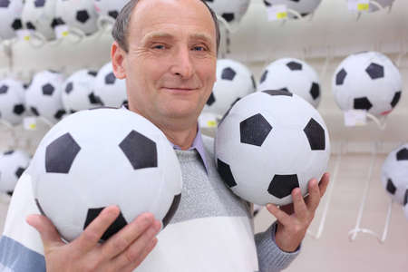 elderly man in shop with footballs in handsの写真素材
