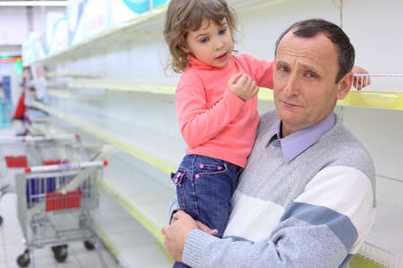  elderly man at empty shelves in  shop with child on hands