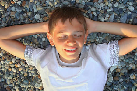 teenager boy lying on stones on stone seacoast, closed eyes, holding hands behind headの写真素材