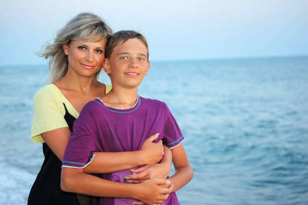 young woman embraces smiling boy on beach in eveningの写真素材