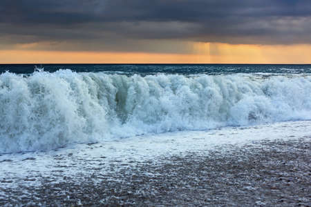 Sea coast with waves, wide angle; sun appeared through cloudsの写真素材