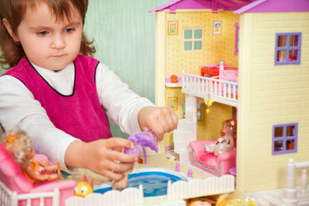 little girl washes a doll in pool of toy house  の写真素材