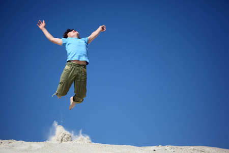 boy jumps on sand with  lifted handsの写真素材