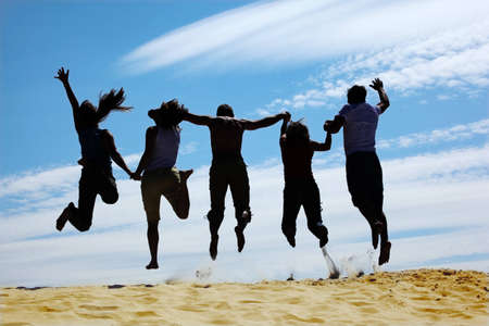 group of friends jumps on sand, rear view, silhouetteの写真素材