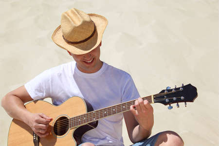 guy in straw hat plays guitar sitting on sandの写真素材