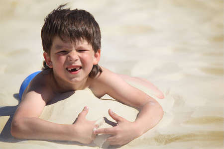 boy without  foreteeth lies on sandの写真素材