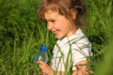 smiling little girl in grass with plastic bottleの写真素材