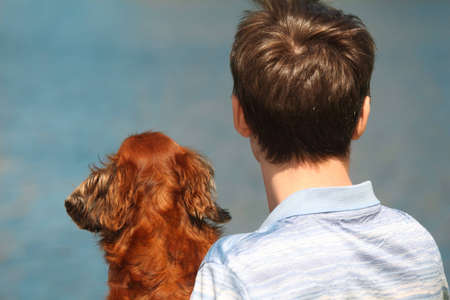 Young man and his dachshund  from back outdoor against waterの写真素材